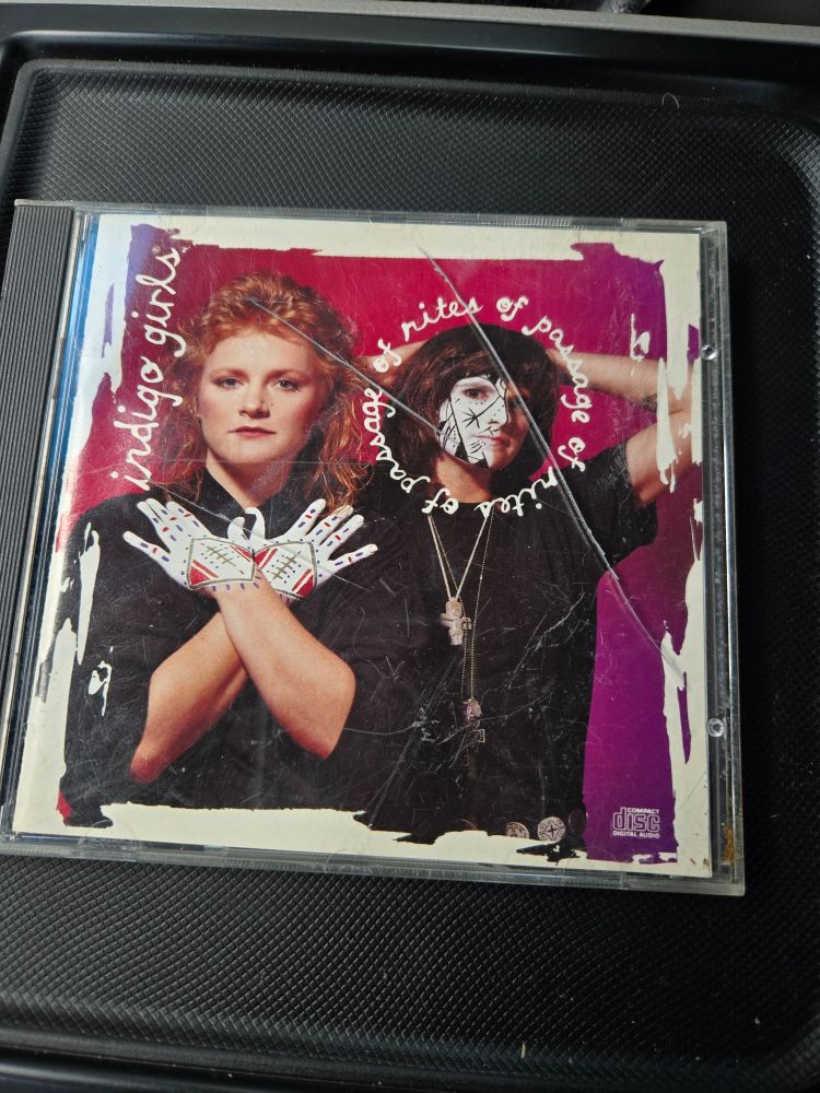 A cracked plastic case with the booklet for the Indigo Girls album "Rites of Passage" showing through the window