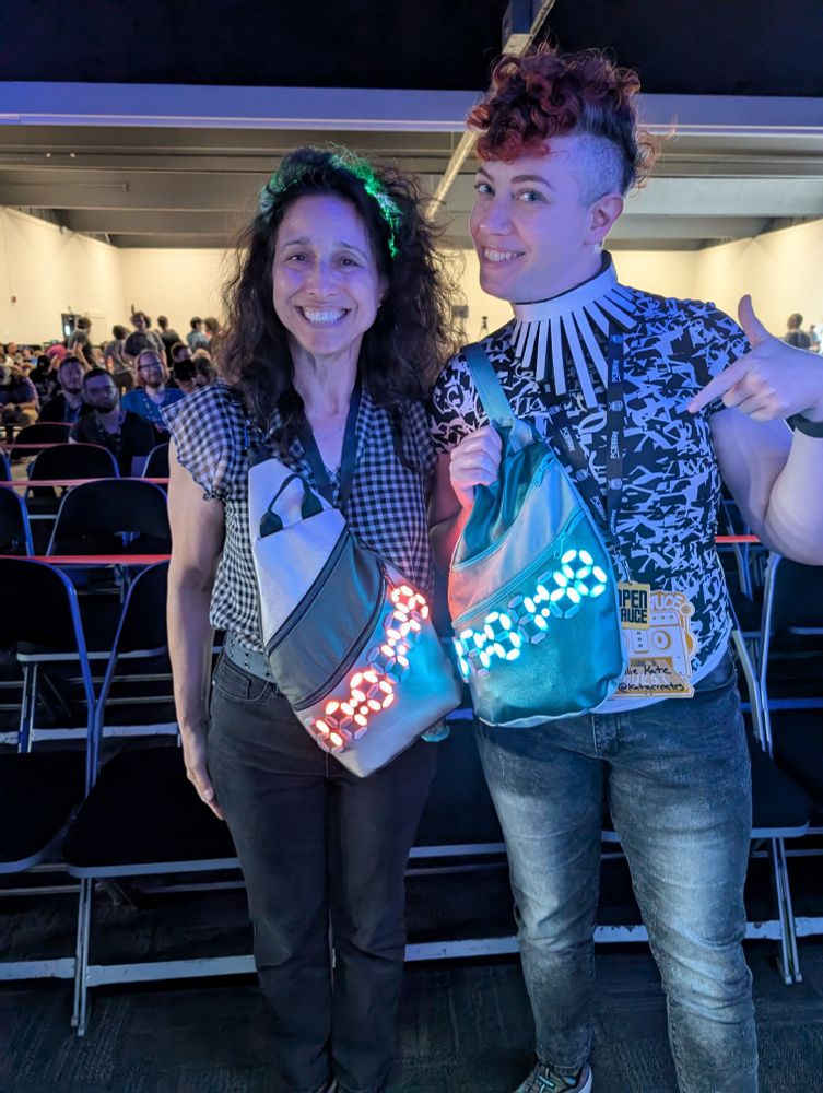 Two very cool makers wearing similar sling bags with illuminated digital clocks on the front 