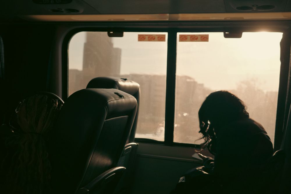 Interior of a train at dusk, with silhouetted seats and a glowing orange sunset framed by trees outside the window.