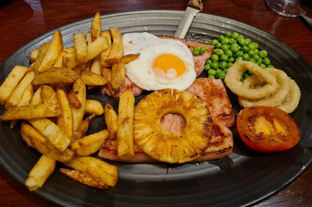 Gammon, chips, egg, pineapple, onion rings, peas and a tomato 