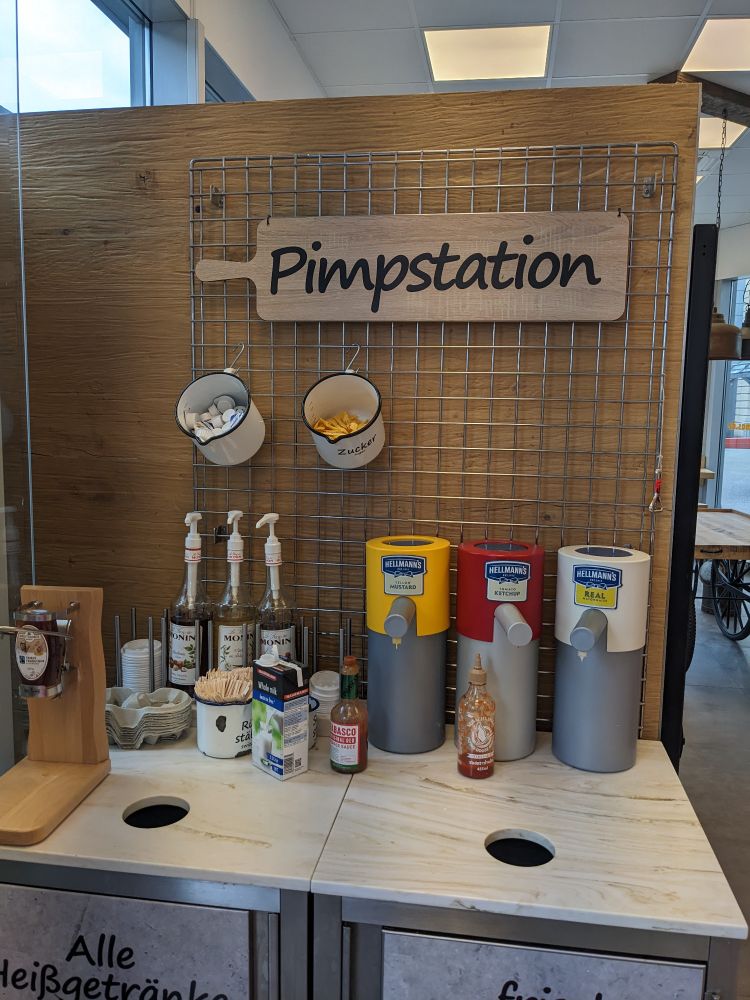 A condiment dispensing station at the München Hauptbahnhof labeled "Pimpstation"