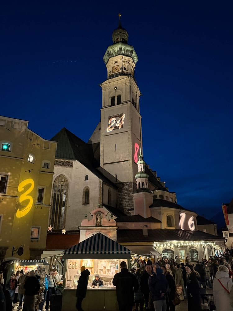 Die Kirche St Nikolaus in Hall vor dunkelblauem Himmel, im Vordergrund erleuchtete Standln 