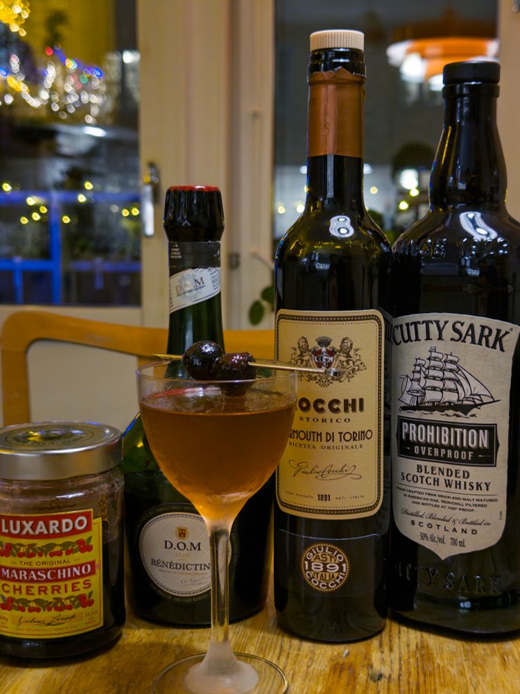 En Bobby Burns cocktail framför flaskor och burk med ingredienser.