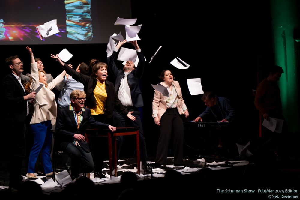 Actors on stage flinging papers into the air, looking distressed