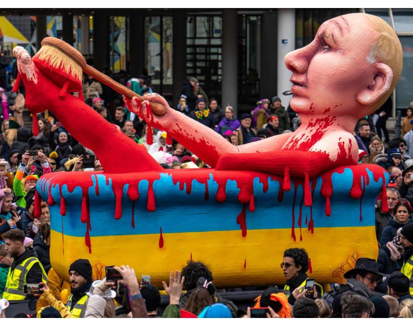 Putin nackt in einer Badewanne mit ukrainischem Blut. Kölner Karneval. Die Skulptur ist umringt von Menschenmassen.  