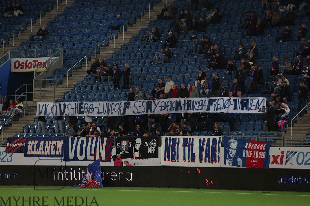 Banner på tribune, signert Volin. Teksten er «vickiUs-hEgg-lindorF-sesAy-enbloM-hAnsen-Fredø-InAuen»