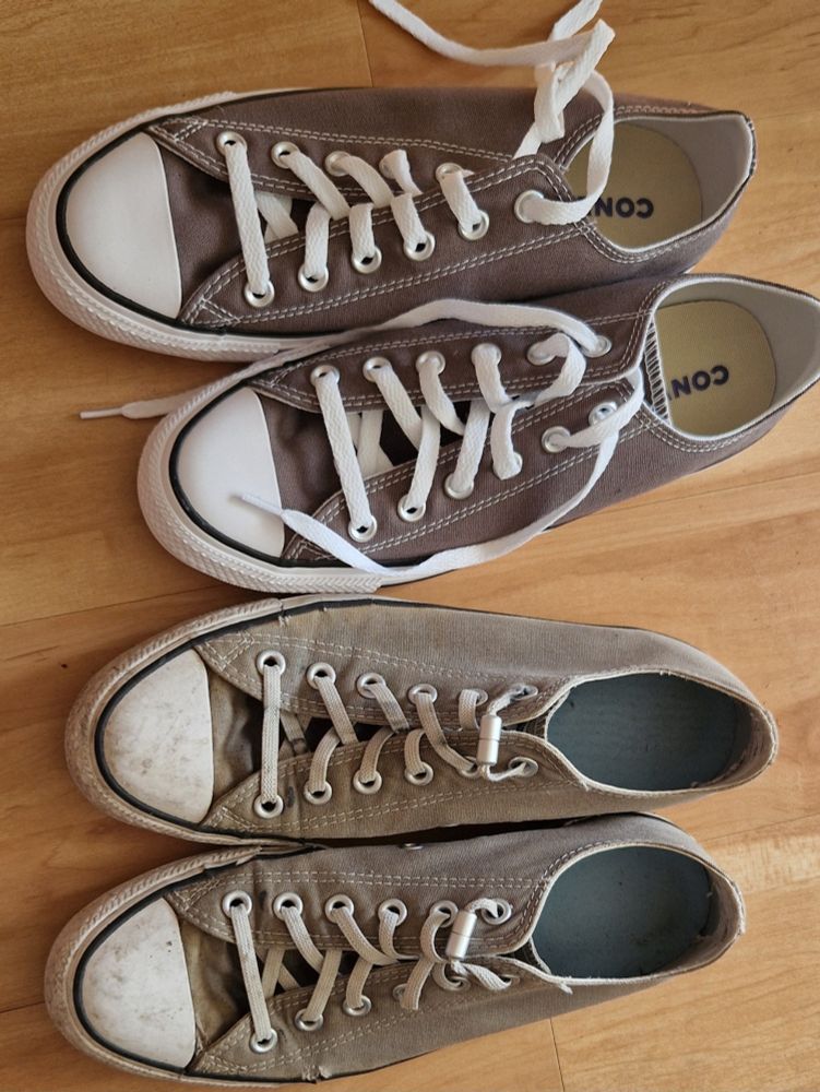 Zwei Paar graue Converse Chucks. Ein Paar komplett neu und ein fünf Jahre altes Paar, das ausgeblichen ist und bereits Löcher hat.