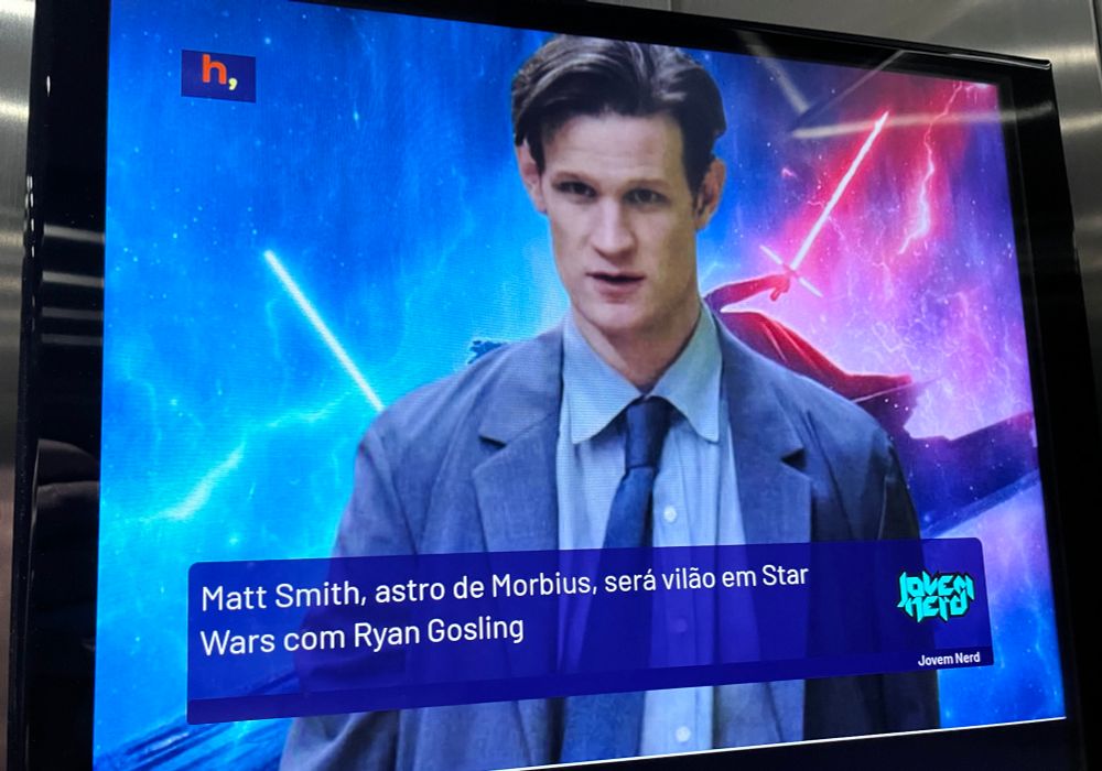Foto de notícia em televisão de elevador com foto do ator Matt Smith sobreposto a um pôster de Star Wars, e o texto “Matt Smith, astro de Morbius, será vilão em Star Wars com Ryan Gosling”