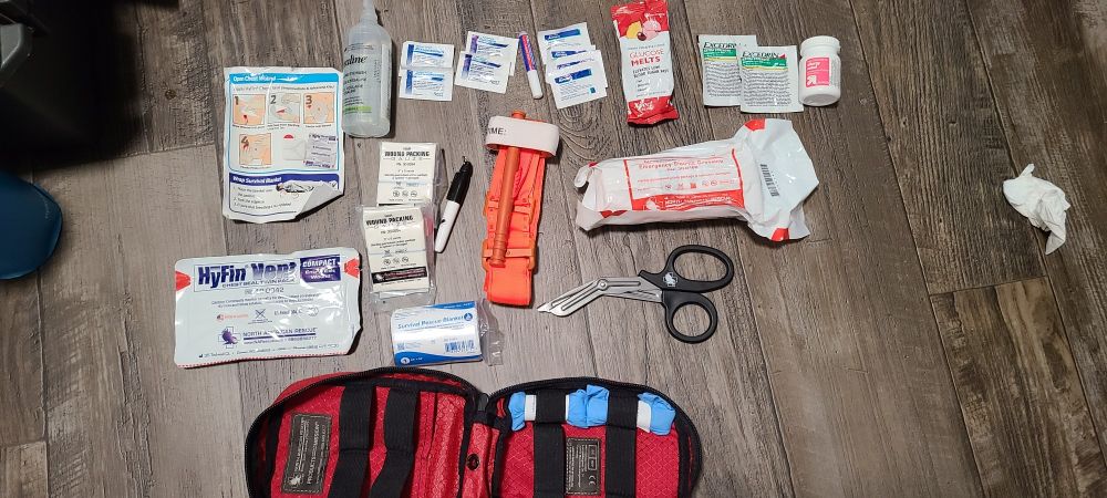 Interior Contents of the IFAK laid out on the floor. There are two types of contents: those that came with the bag, and those added by this user.

Included: Trauma dressing, 2x wound packing gauze, 2x nitrile gloves, Trauma sheers for cutting clothing, "hyfin" brand chest seals for gun shot wounds, a Tourniquet, an emergency blanket to prevent hypothermia, a sharpie to write time of Tourniquet application.

Additions: Glucose, ibuprofen, Tylenol, excedrin, asprin, saline, benadryl, liquid bandage. 

All of these items fit in the IFAK bag. 