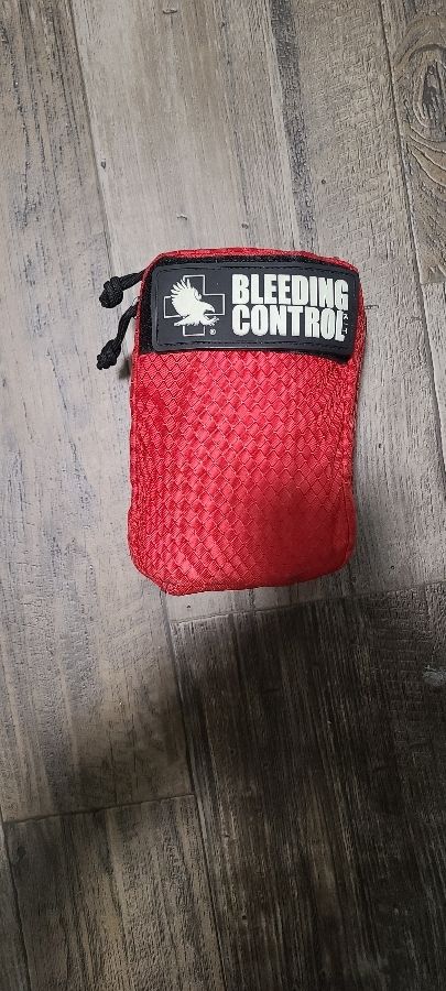 Exterior shot of an Individual First Aid Kit. It is a red, 3"x6" nylon bag with the exterior label "Bleeding Control"