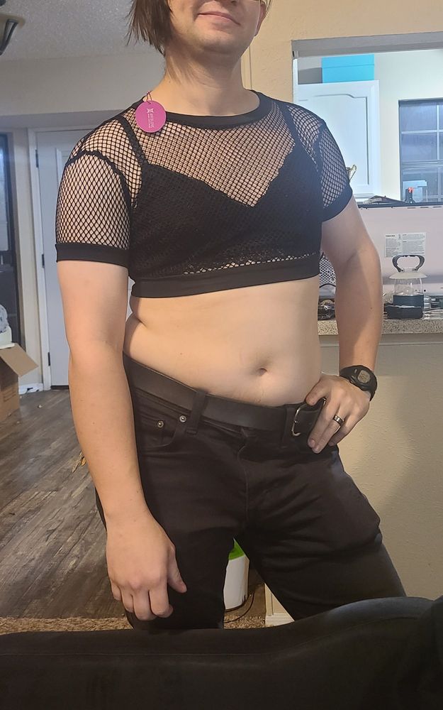 Transfem enby wearing black Jeans, Bralette, and a Black Fishnet Crop top. 