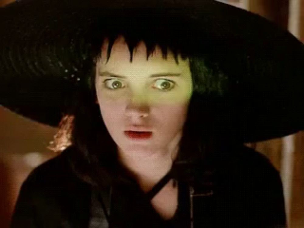 a woman wearing a black hat with green eyes is making a funny face .