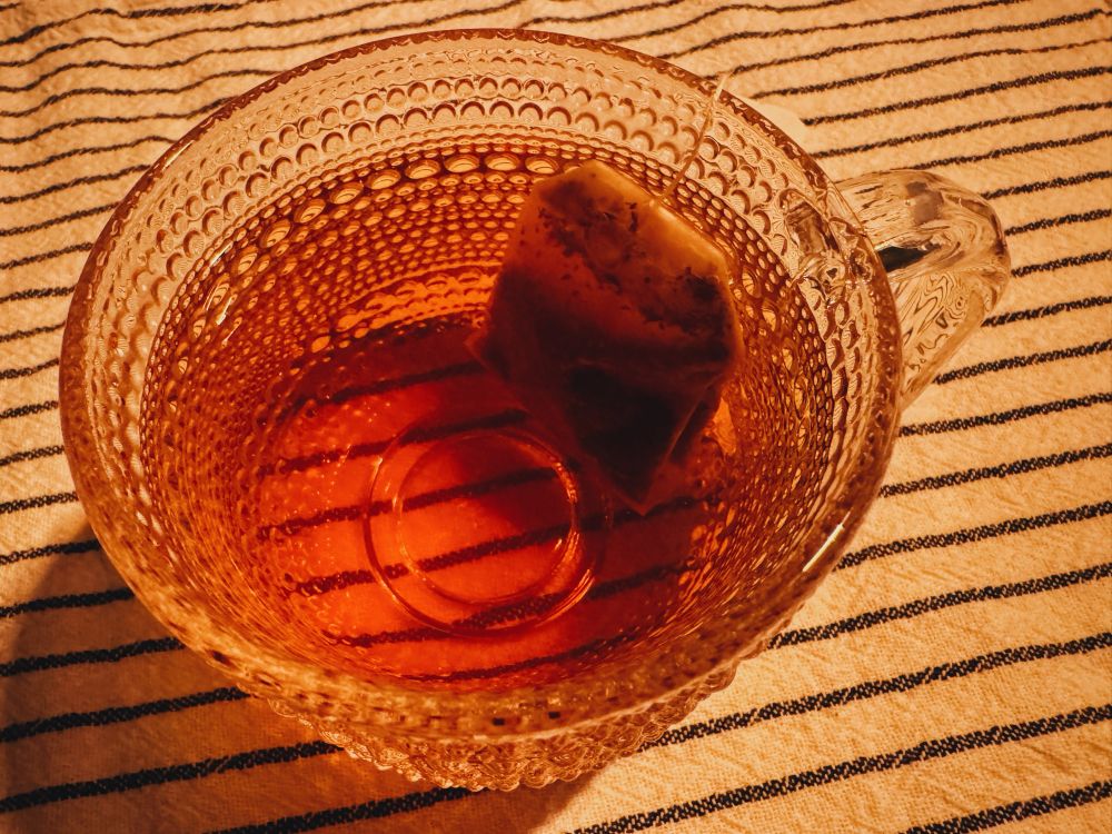 ガラス製のマグカップに入った薄茶色のお茶とティーバッグ。