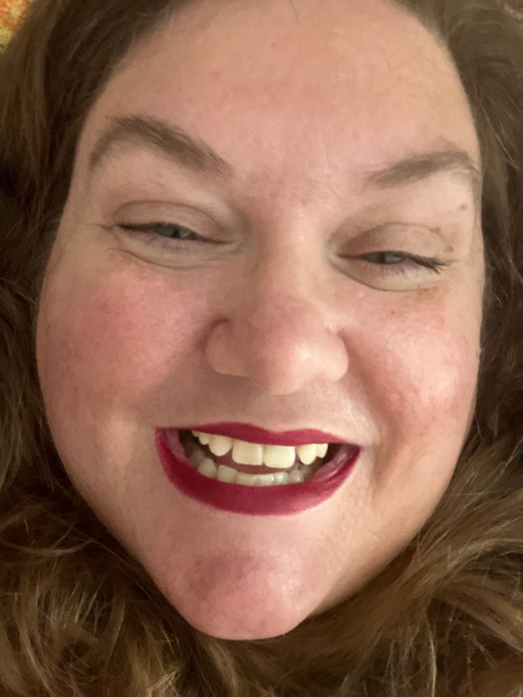 a white person with long hair, green eyes, and burgundy lips 