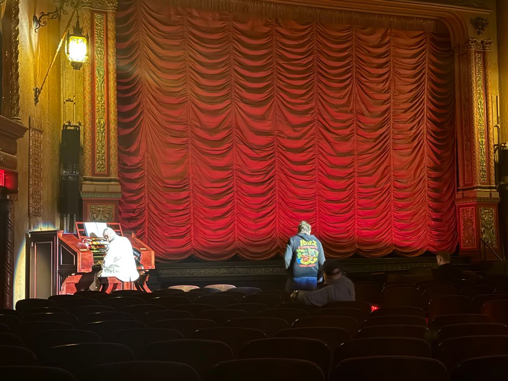 The red curtain covering the screen at the Music Box in Chicago. On the left a bald man plays the organ. 