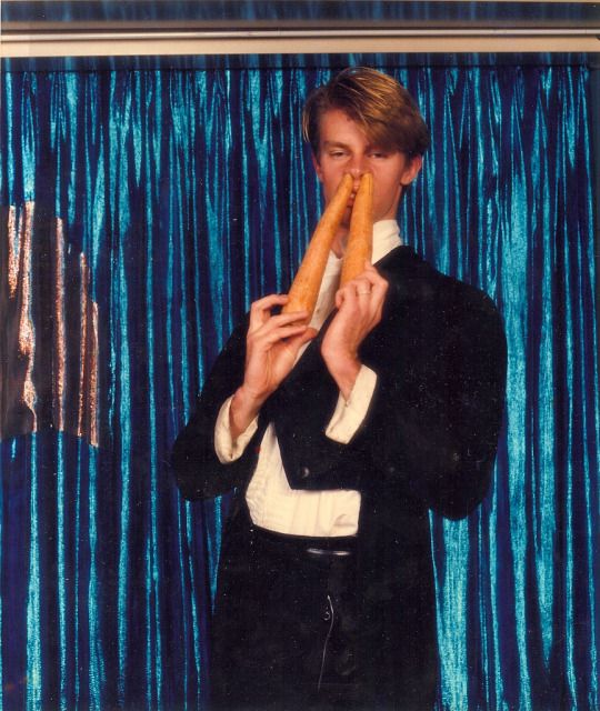 A man in a tuxedo sticking two large carrots into his nostrils 