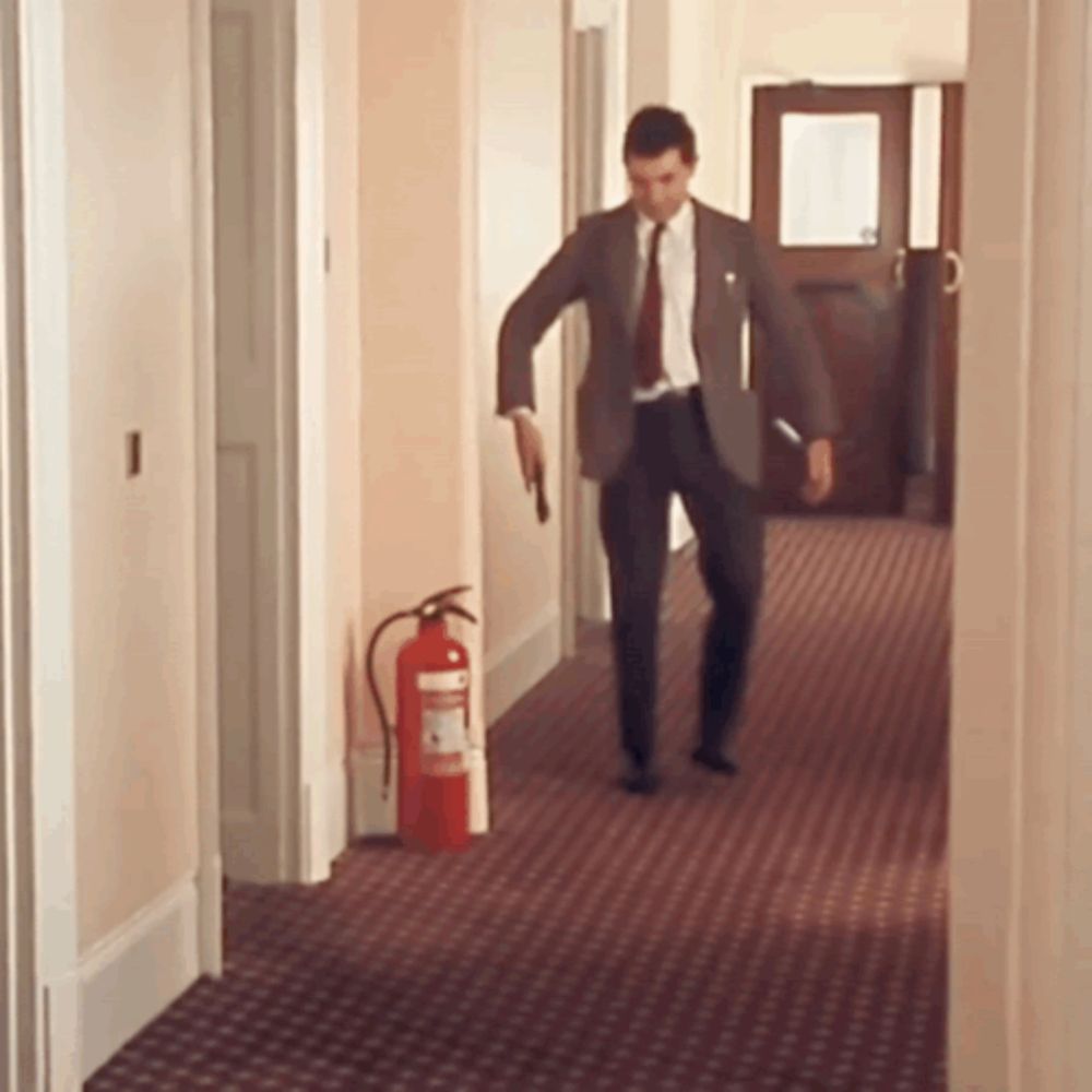 a man in a suit and tie is walking down a hallway with a fire extinguisher in the background