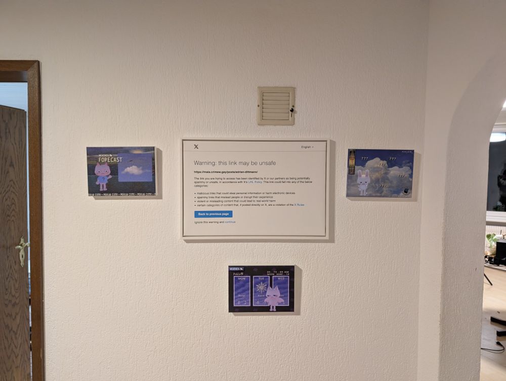 a photo of a wall, in the middle is a framed canvas print of a twitter "this link may be unsafe" popup, it is surrounded by three more way smaller canvas prints of art from the game peklo