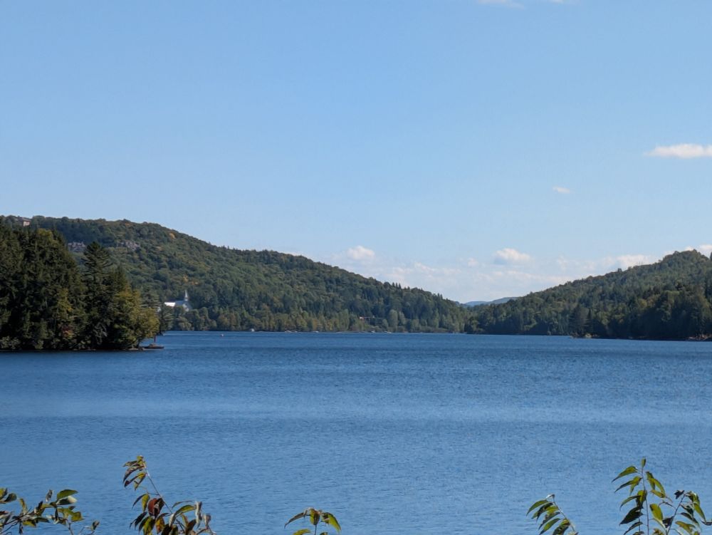 Low mountains descend on either side to a placid, blue lake. The valley continues beyond the lake right of center. Left of center, on the far shore, is a light-grey church.