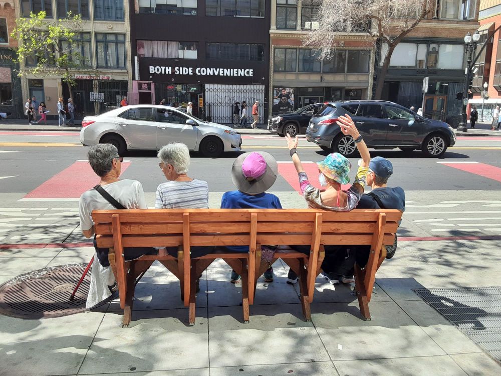 Five elders sitting on a handmade bench at a bus stop in Oakland