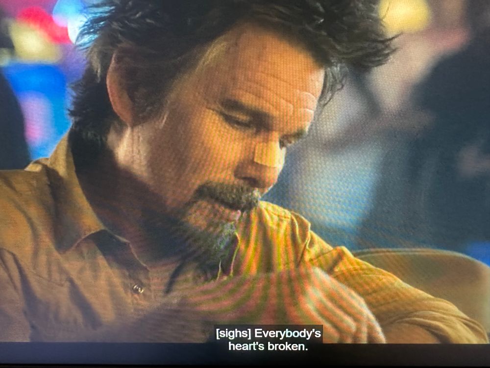 Ethan Hawke, disheveled and with a bandage across the bridge of his nose in a bar. The subtitle reads, 

[sighs] Everybody’s heart’s broken.
