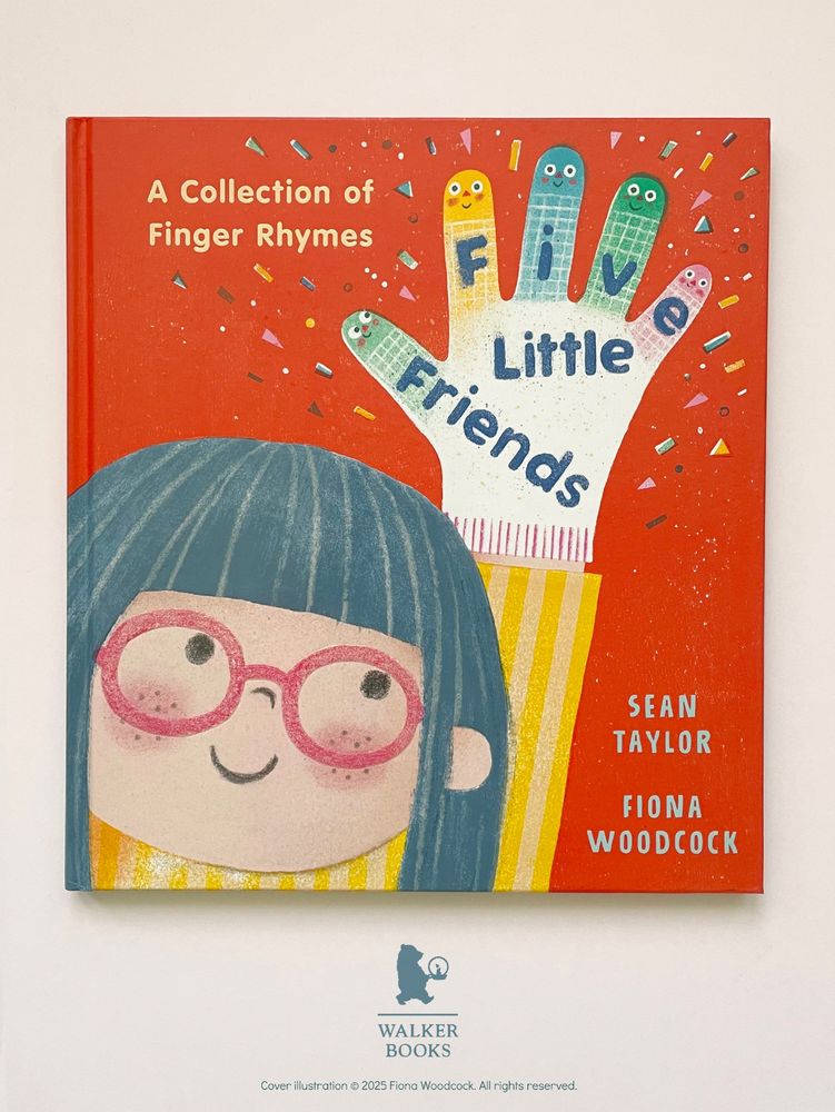 A photo of the hard back UK version of FIVE LITTLE FRIENDS: A Collection of Finger Rhymes, by Sean Taylor and Fiona Woodcock. A dark orange cover with a happy girl with pink glasses holding up a hand wearing a colourful glove. Each of the five fingers of the glove has a happy smiley face on it.