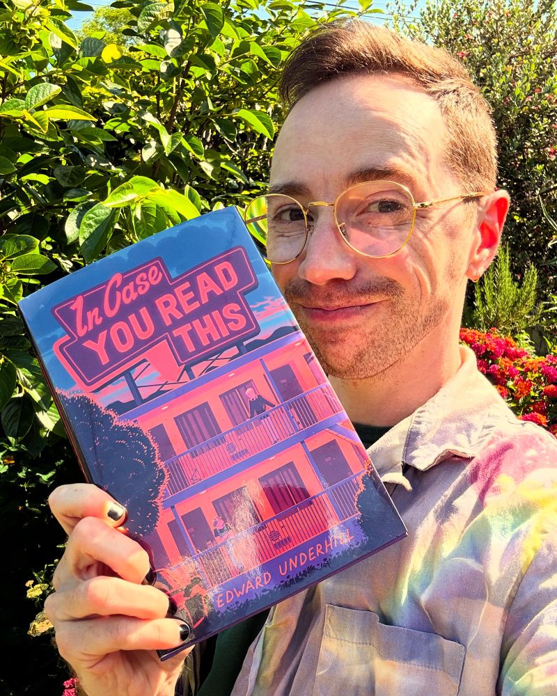 The author, a white trans man with glasses, holds a copy of his new YA book, In Case You Read This.