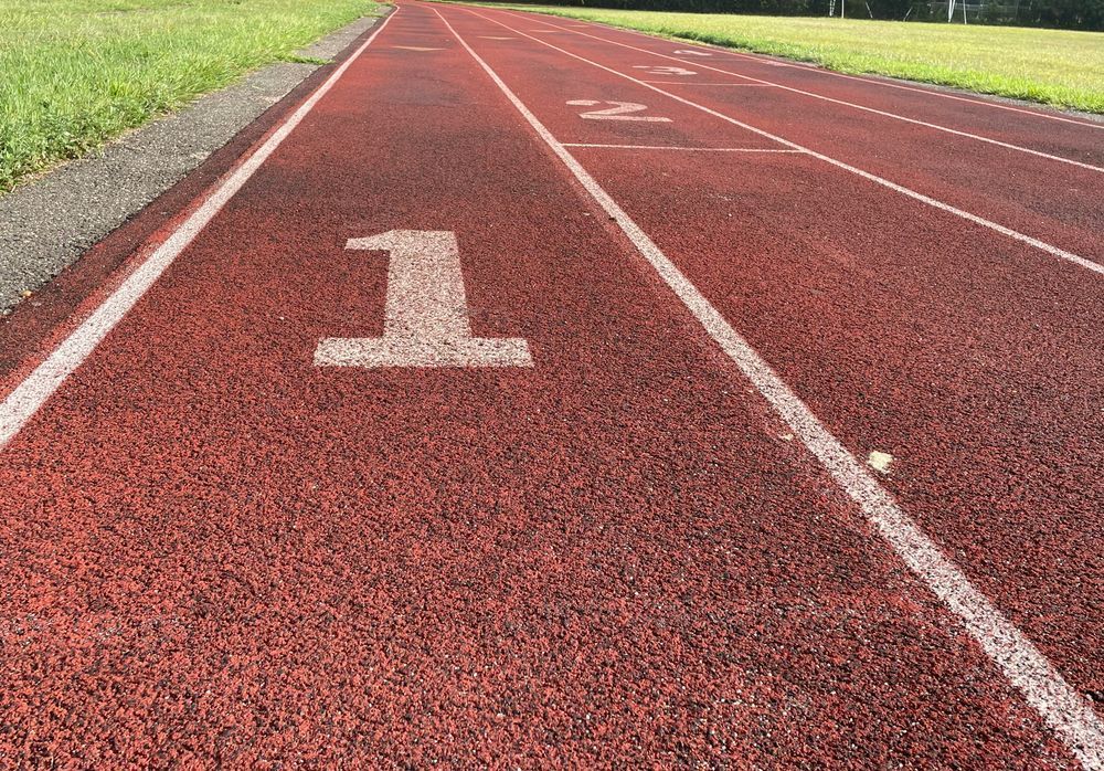 A run track with four lanes. The first one is in focus, the tarmac is red and the lines between the lanes are white, with big white numbers on each track. Photo by Aleksandar Pavlovic on Unsplasch
      
