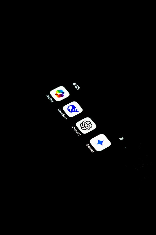 A dark phone screen on a black background. On the screen there are four app icons, Copilot, Deepseek, ChatGPT and Gemini. Photo by Saradasish Pradhan on Unsplash

