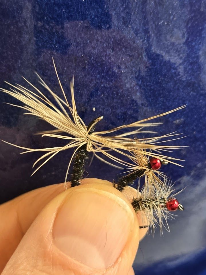 Three fishing flies held in fingers in front of blue glazed pottery