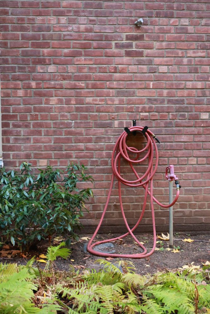 a red hose wrapped up on a red brick wall with some green plants in the foreground