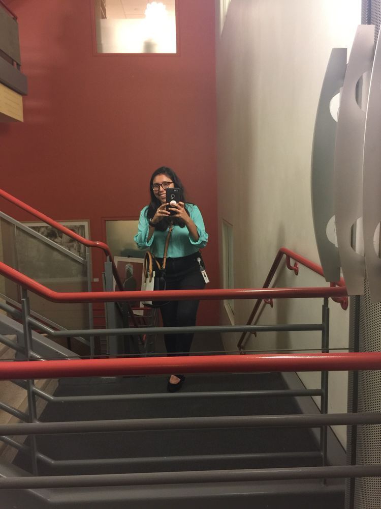 Mirror selfie of me in 2017 on the old Scholastic stairs on my first day of work ever. I’m wearing a teal top, black pants, and black heels smiling as I take the pic. 