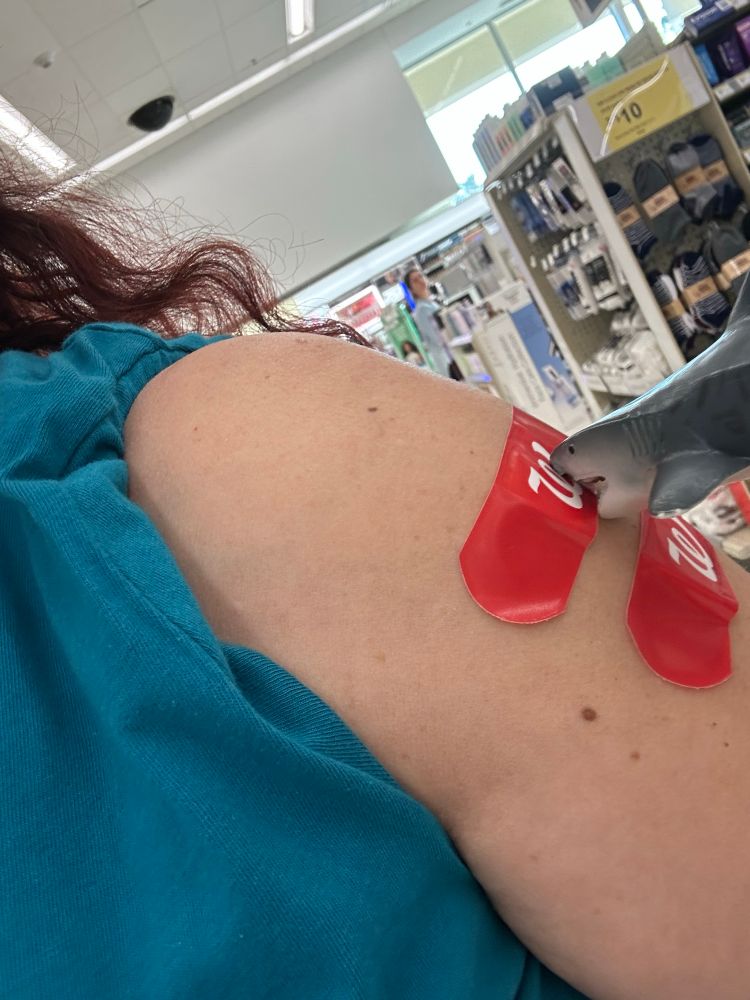 Arm with two vaccine bandages. A toy shark is attacking a bandage. 