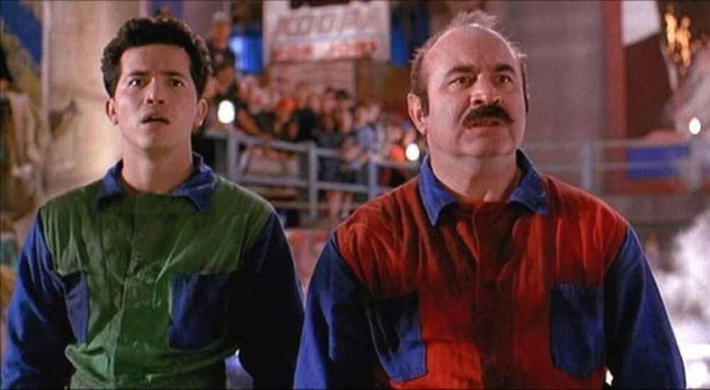 john leguizamo and bob hoskins in the 1993 smash hit super mario bros live action movie. john is dressed in a green jumpsuit and bob is dressed in a red jumpsuit, and their facial expressions are shocked and dismayed.