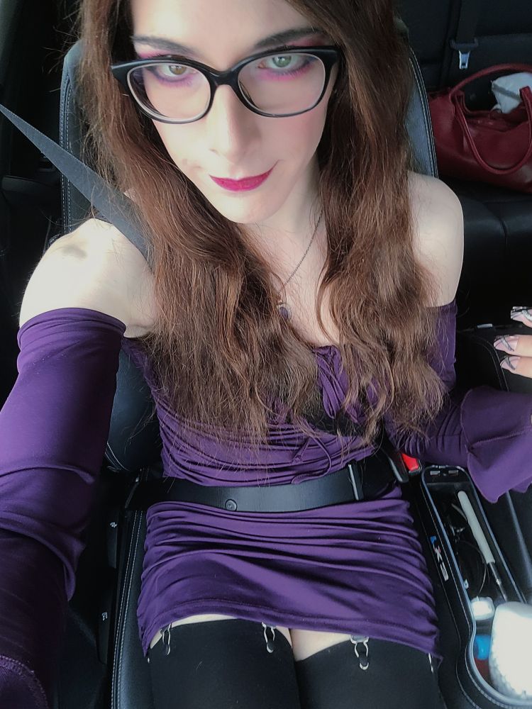 Trans Girl in a purple dress sitting in a car, passenger seat.