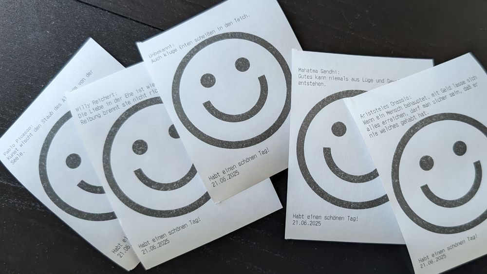 Ein paar Ausdrucke aus einem Bondrucker mit einem großen Smiley und einem Spruch des Tages.
