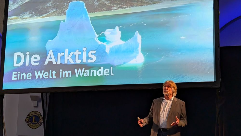 Arved Fuchs berichtet über die Arktis. Im Hintergrund ist eine Folie mit dem Text "Die Arktis. Eine Welt im Wandel" zu sehen.