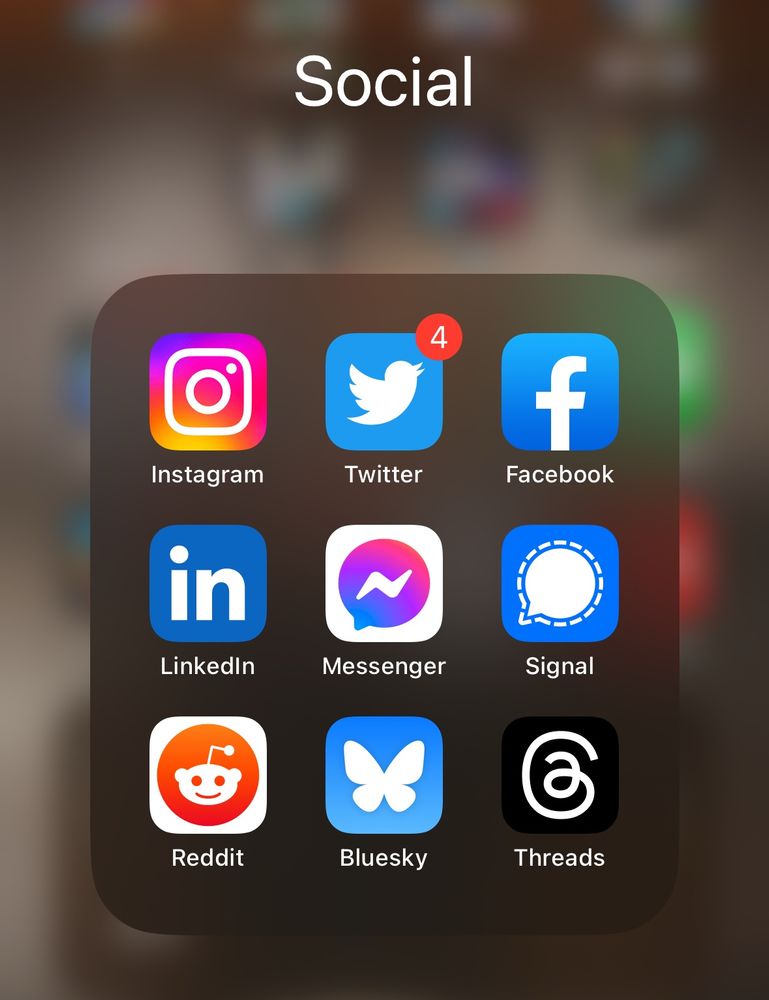 Screen shot of an iPhone app folder of social media icons. Twitter is the old blue and white bird icon. Bluesky is the blue and white butterfly. 