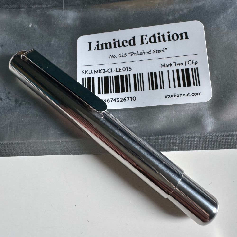 A polished steel pen rests on a resealable black-and-grey pouch labeled “Limited Edition.” The label reads: “No. 015 ‘Polished Steel’,” with additional product info: “SKU: MK2-CL-LE015,” “Mark Two / Clip,” and a barcode with the number 73674326710. The pen is sleek and reflective, with a minimalist clip design. The website “studioneat.com” appears at the bottom of the label.
