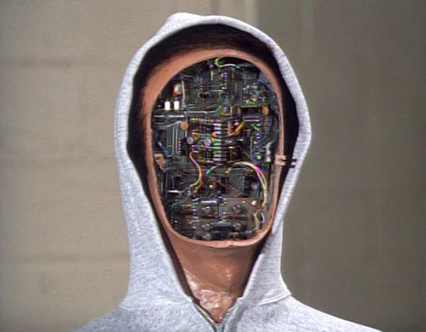 A humanoid robot wearing a light gray hoodie, with its faceplate removed to reveal intricate circuits and wiring beneath. This image is from the Six Million Dollar Man episode titled “Day of the Robot,” featuring a lifelike android antagonist with a synthetic outer appearance concealing its mechanical interior.