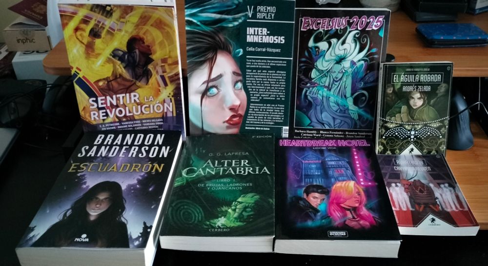 Escritorio con dos filas de libros. Una con los libros en vertical (arriba): Sentir la revolucion, Inter-mnemosis, Excelsius 2025 y El águila robada.
Otra con los libros tumbados(abajo): Escuadron, Alter Cantabria, Heartbreal hotel y Ruha|Alma
