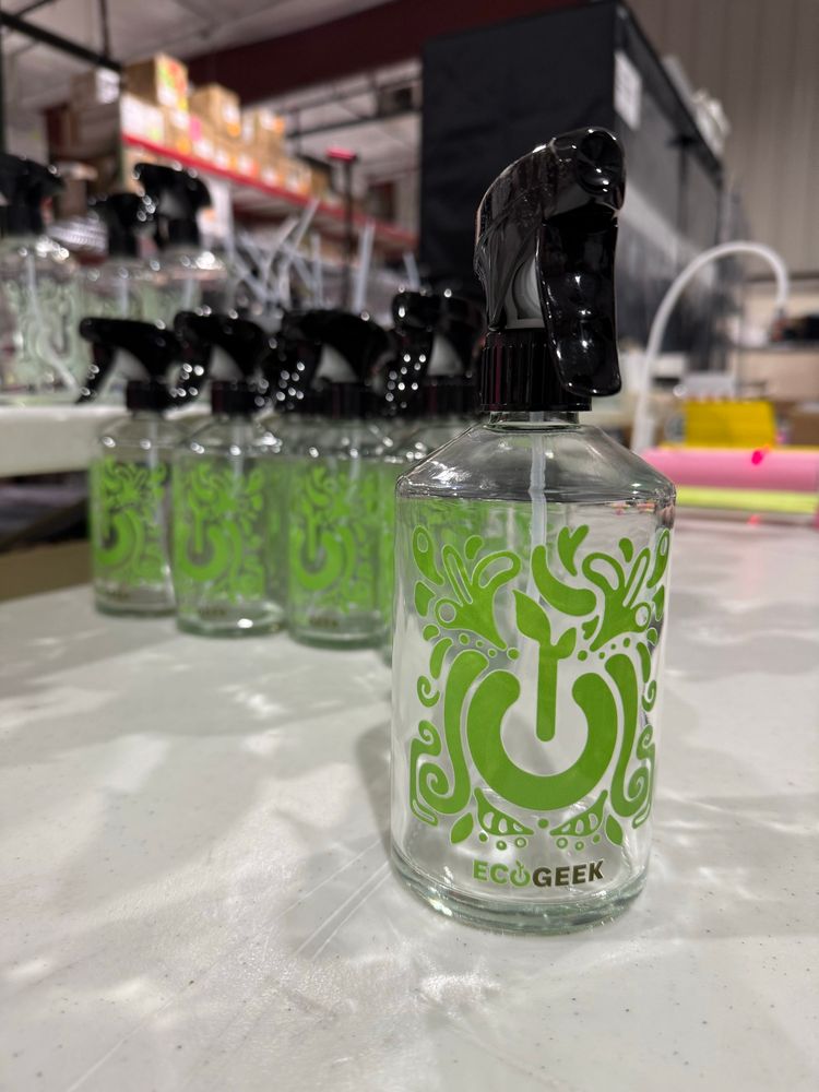 Glass cleaning bottles with green, plant-themed EcoGeek logo on them.