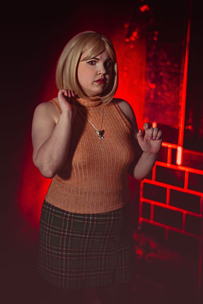 Linds is standing in a creepy brick room, with ominous red lighting in her Ashley Graham cosplay 