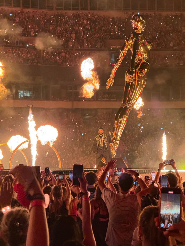 A man on stage in front of a gold statue surrounded by flame