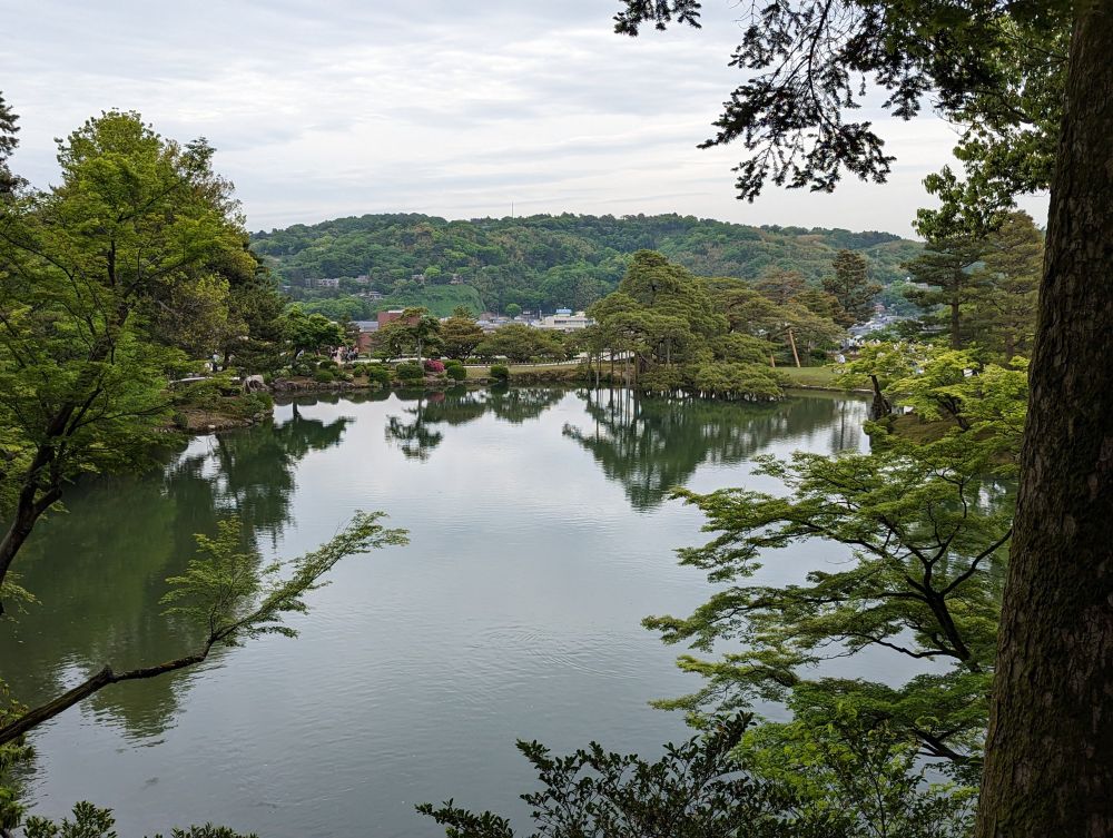 kenroku-en garden: lake with soft mountains behind. Trees reflect in the lake's mirrorlike surface.