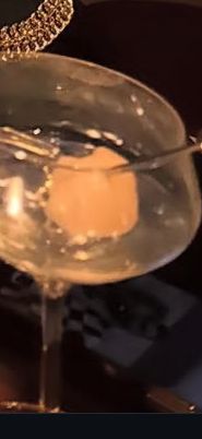 A cocktail glass with a phone near it that has a blurry picture of Taylor Swift and Travis on the lock screen