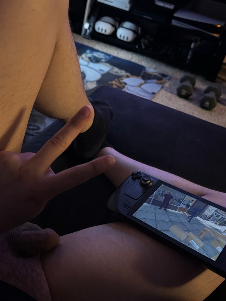 Naked legs, soft cock flopped to the right side. Steam deck on right leg, supermarket simulator on the screen. 