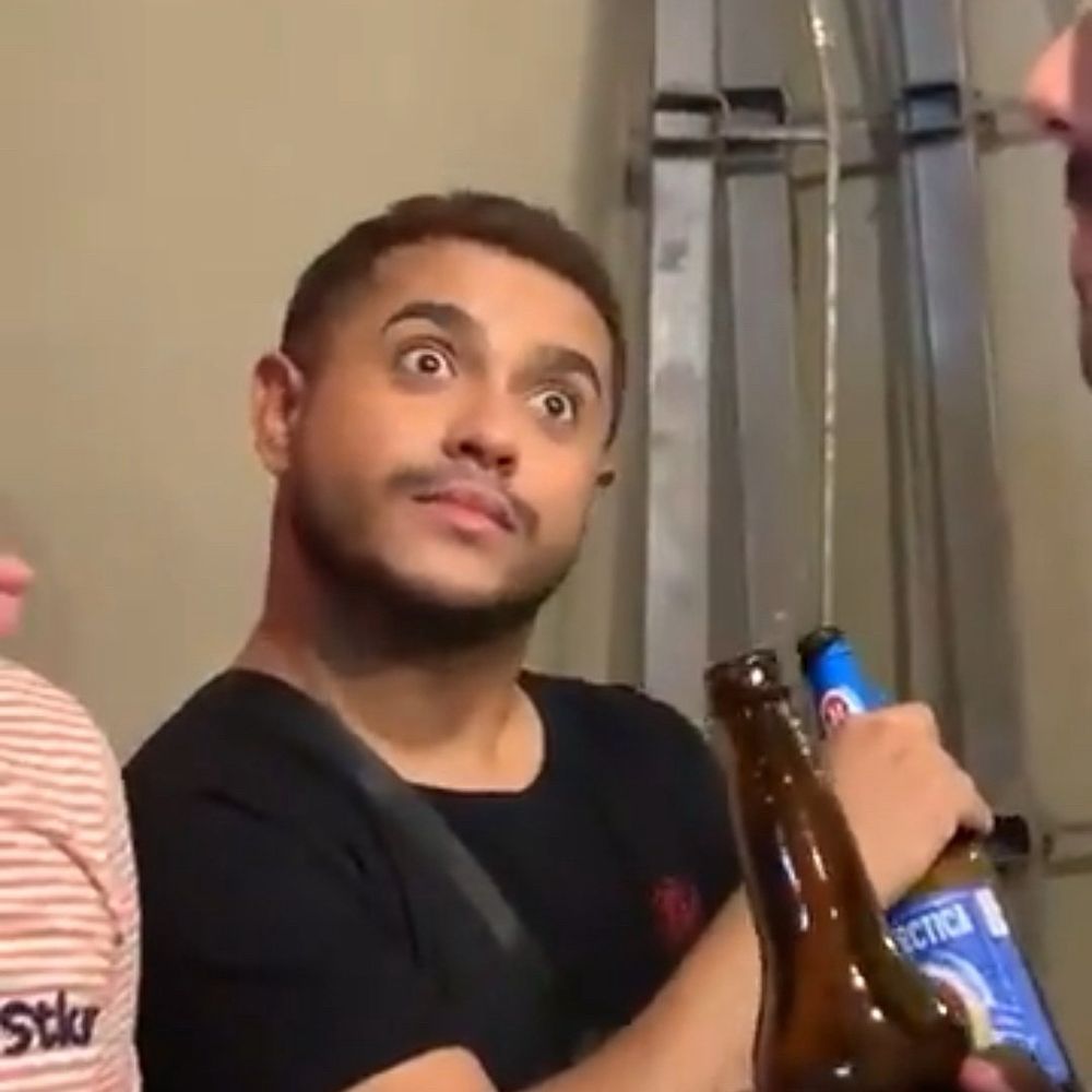 Homem com olhos arregalados segurando uma garrafa de cerveja com uma expressão de choque/surpresa.