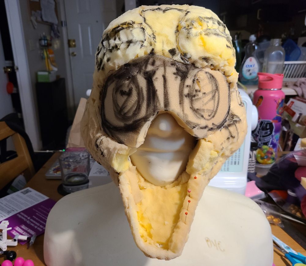 Picture of a fursuit foam headbase, with a large hole in the mouth region which is exposed due to no upper muzzle is attached. A stern mannequin mouth sits exposed and unamused. There are two large, kawaii esque eyes scribbled where the future follow me eyes will be placed.