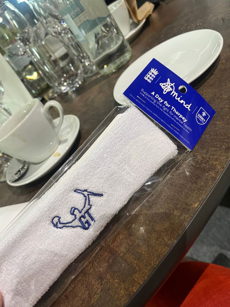 A white towelling headband with a silhouette of Graham Thorpe raising his bat. The headband is in clear wrapping with a blue Mind tag which has England cricket and Surrey logos on. 